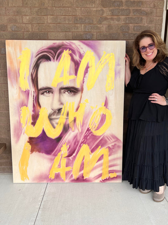 Woman standing next to a large painting with motivational text and a portrait.