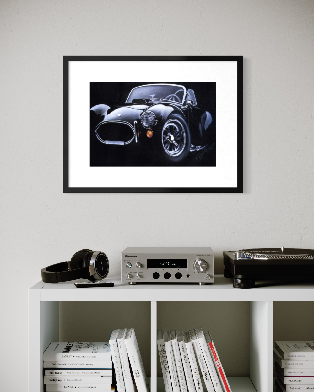 Framed black and white car print on a wall above a shelf with books and a radio. ac cobra limited edition paper fine art print reproduction by shenshen.