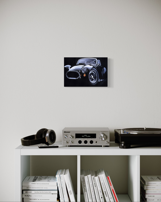 Framed picture of a classic car on a wall above a shelf with electronic equipment and books. ac cobra limited edition canvas giclee fine art print reproduction by shenshen.