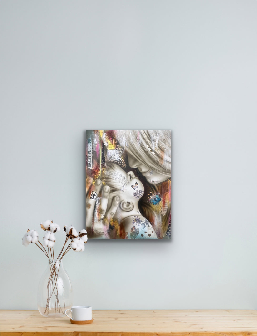 Abstract art piece on a wall above a wooden table with a vase and cup.