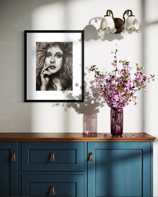 Framed artwork on a wall above a blue cabinet with a vase of pink flowers. Stevie Nicks by ShenShen limited edition reproduction canvas giclee fine art print.
