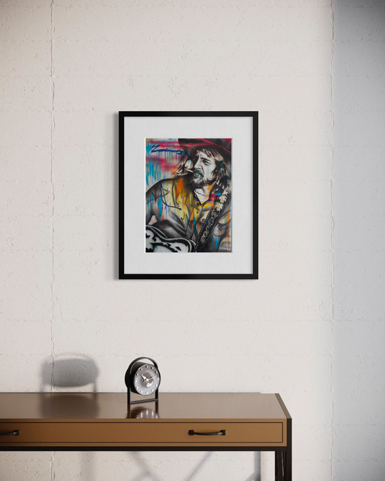 Framed artwork on a white wall above a wooden desk with a clock. Waylon Jennings limited edition reproduction fine art print by ShenShen.