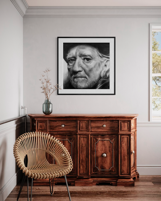 Wooden sideboard with a framed portrait above it in a room with a wicker chair. Willie Nelson limited edition reproduction fine art print by ShenShen.